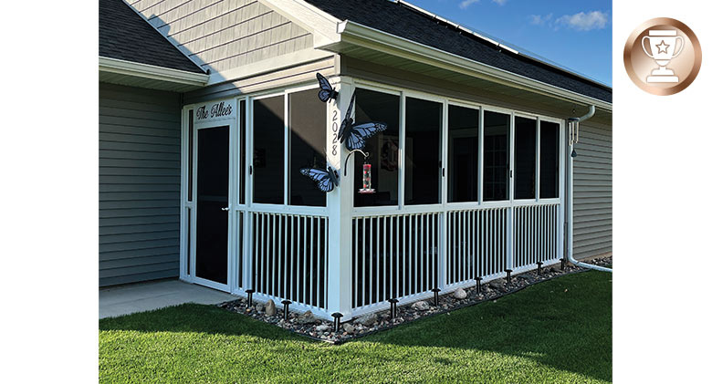 A patio enclosed with a white screen room with picket railing fence and storm door entry; decorated with butterflies.