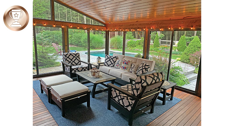 The interior of a glass sunroom with comfortable furniture and a view of the outdoor pool and landscaped yard.