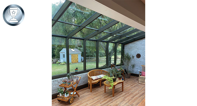 Interior of a solarium with stone knee wall and glass roof, wicker furniture and several plants.