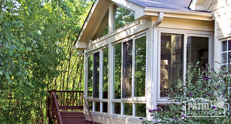 Sandstone four season sunroom with vinyl frame and glass knee walls enclosing an existing screened porch.