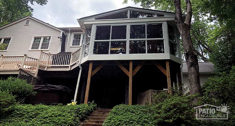 Looking up at a home on a hill with a gable-roofed sunroom on the second story. A large deck attaches to the sunroom.