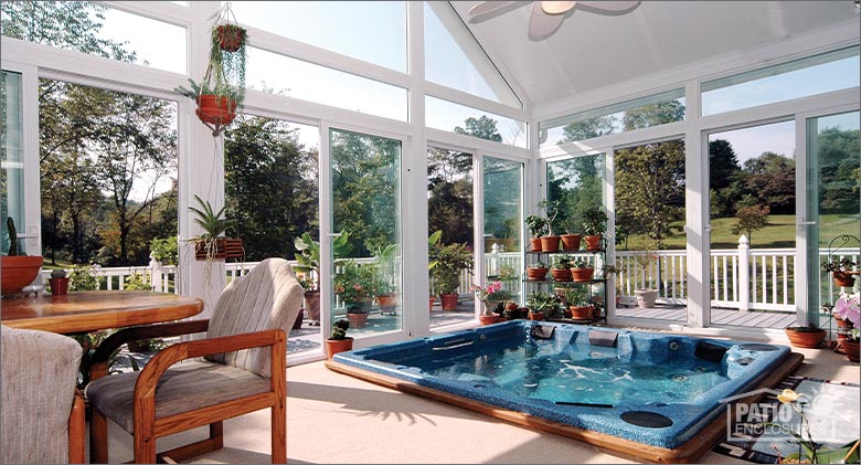 Sunroom interior with lots of plants, table and chairs, ceiling fan and a blue hot tub at floor level.