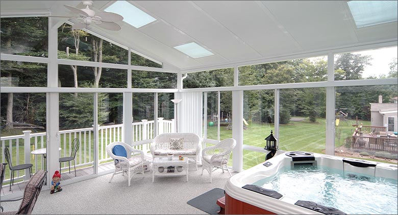 White sunroom interior with glass roof panels, seating area in the corner and a white hot tub in the foreground.