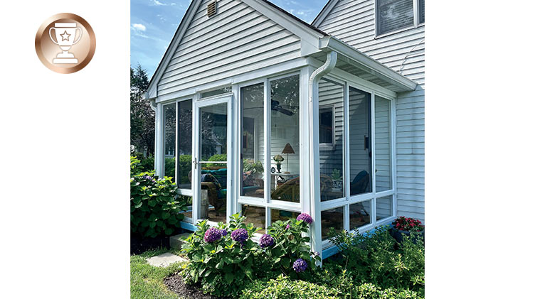 A patio with gable roof enclosed with glass with a storm door in the middle.