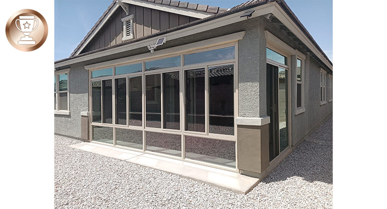 A neat tan home with a glass-enclosed corner patio and gravel all around.