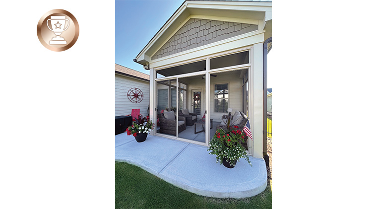 A screened-in patio with gable roof and two potted flowering plants in front on curved concrete patio