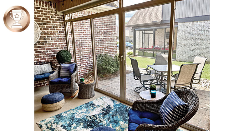 A seating area with blue cushions inside a glass-enclosed patio with a view of an outdoor table and the house next door.