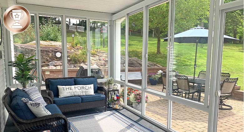 The interior of a glass-enclosed patio furnished with two loveseats. View of the outdoor patio and nicely landscaped yard.