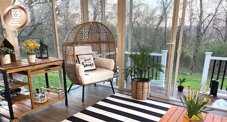 Interior of a sunroom featuring a rounded cushioned chair, black and white striped carpet, and daffodils on coffee table.