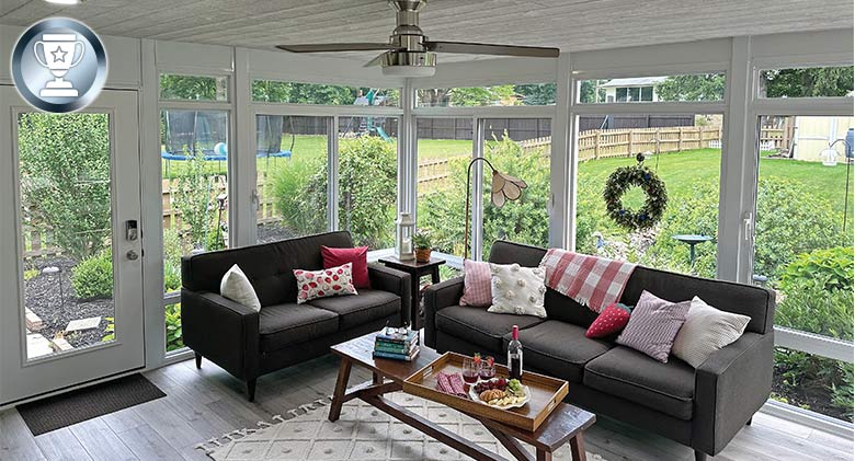 Sunroom interior with a brown sofa and loveseat, lots of pillows, and a coffee table with a tray of snacks and drinks.