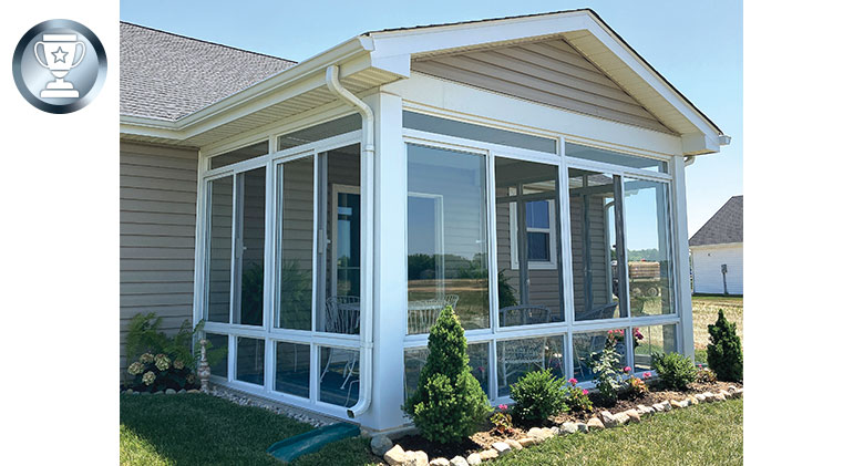Glass-enclosed patio with a gable roof and glass knee wall. Neatly landscaped around the perimeter.