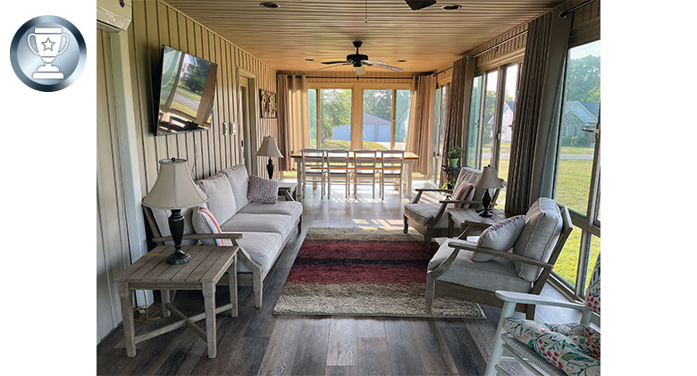 Interior view of a long sunroom with comfortable seating area and dining table and chairs, area rugs.