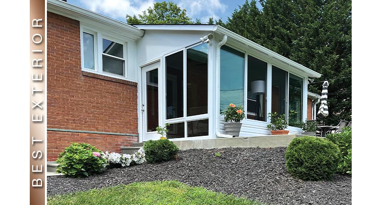 Look up at the exterior of a white three-season patio enclosure with single-sloped roof on a brick home.