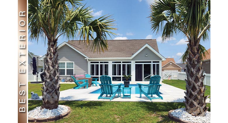 Two palm trees frame a photo of a glass patio enclosure with a pool and aqua-colored Adirondack chairs in front.