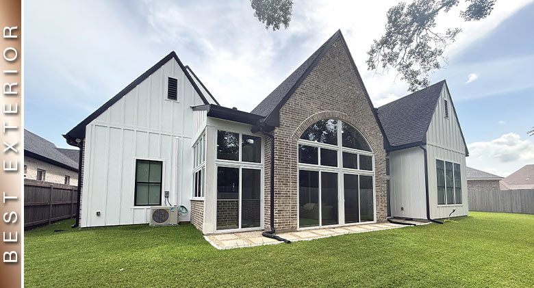 : A farmhouse-style white home with black trim. A covered patio in the center has brick fascia and is enclosed with glass.