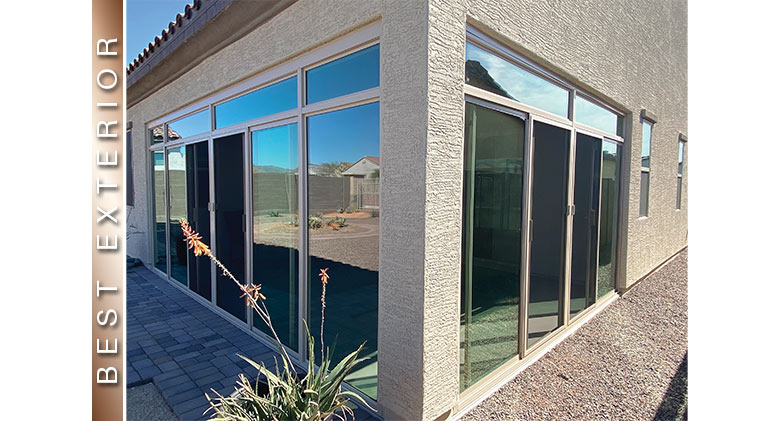 The exterior of a tan stucco home with a glass-enclosed corner patio and an orange flower in the foreground.