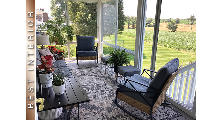 Interior of a three-season sunroom furnished with blue chairs and sofa, a side table, rug, and plants.
