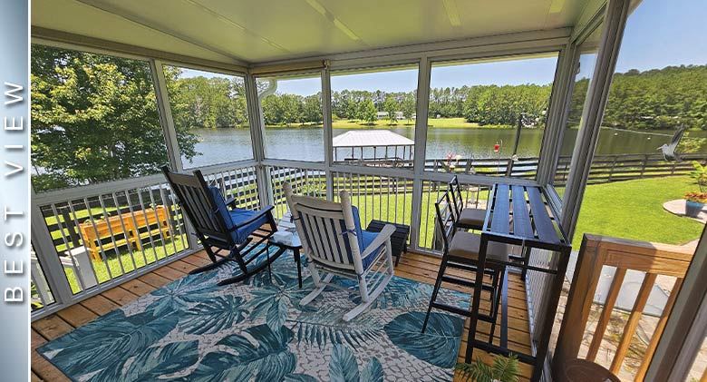 Rocking chairs with blue cushions, blue print rug, and tall table with chairs in screen room with railing overlooking a lake.