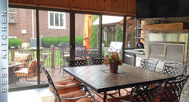 Earthtones decorate this outdoor kitchen sunroom with fireplace and a large table and chairs.