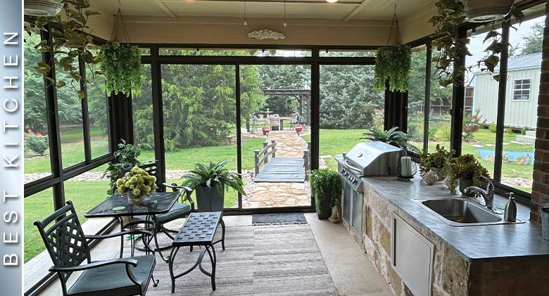 Wrought iron table, chairs, and bench with many plants in an outdoor kitchen screen room.