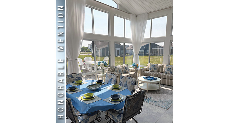 The interior of a glass patio enclosure with white tied-back curtains, a seating area, and a set table and chairs.