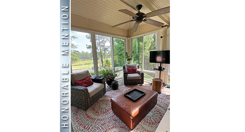 Interior of a sunroom with a view furnished with two wicker chairs with thick tan cushions and red pillows, tv, coffee table.