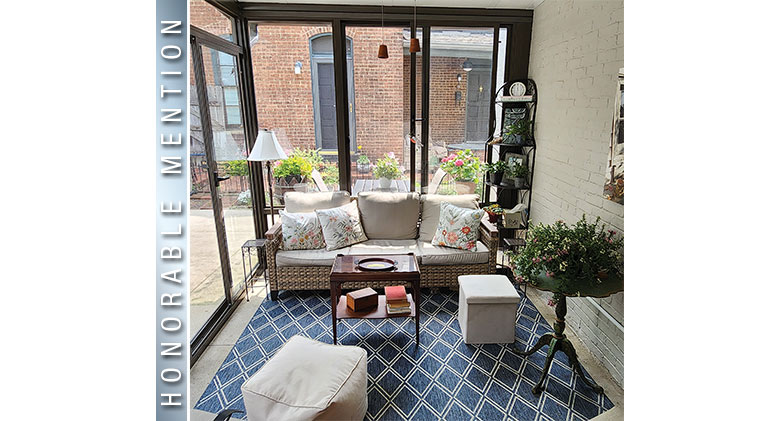 Blue and white geometric rug in a glass sunroom with sofa, two ottomans, small table, and various tables and plants.