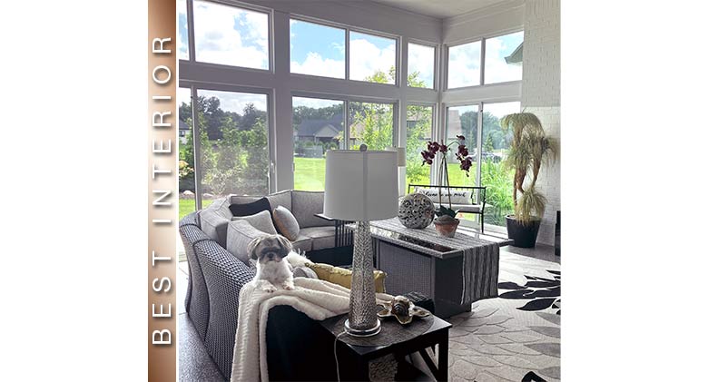 Best Interior: Small dog on the back of an L-shaped sofa in a sunroom with soaring glass walls.
