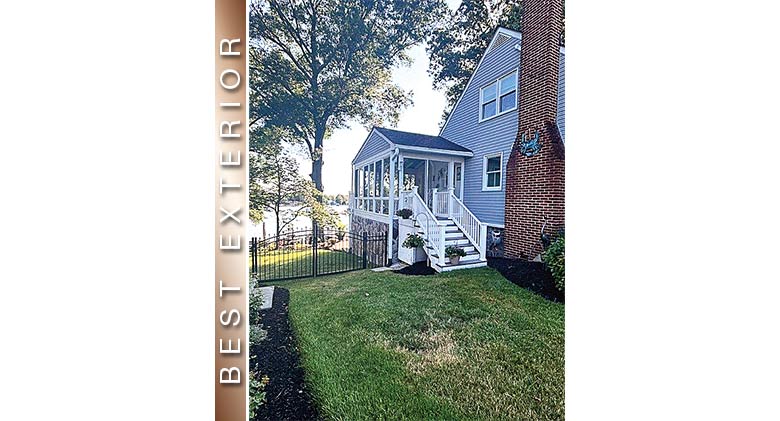 Best Exterior: White three-season porch enclosure with gable roof on gray house on a lake.
