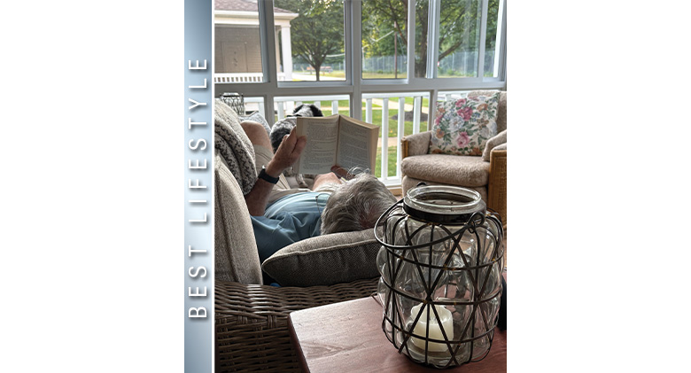 Best Lifestyle Photo: A man reclining on a sofa with dog at his feet reading a book in a three-season sunroom.

