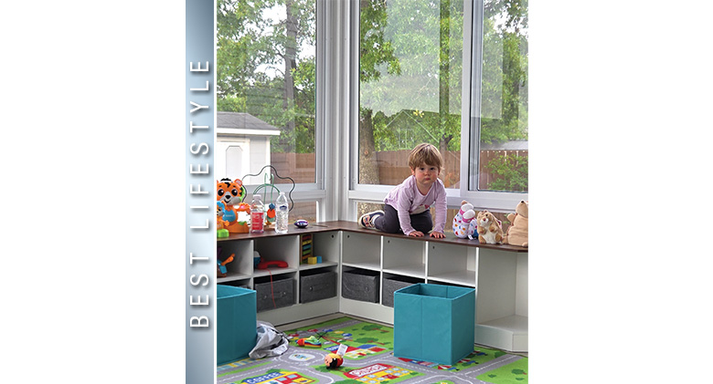 Best Lifestyle Photo: A toddler crawling on the top of low shelves filled with toys in a glass three-season sunroom.

