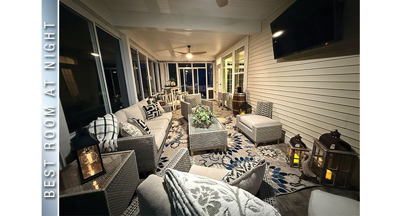 Best at Night: Lit interior of a three-season patio enclosure with seating and dining areas, TV mounted on the wall.
