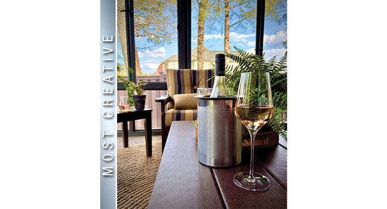 Most Creative Photo: Still life of wine glass, wine bottle on wood table with striped chair and glass wall of sunroom.
