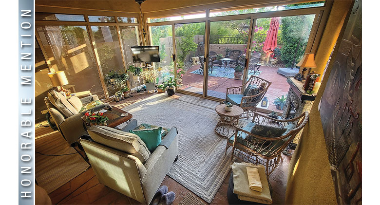 Honorable Mention: Sunlight streaming into a three-season patio enclosure with throw rug, comfortable seating, TV,
plants.