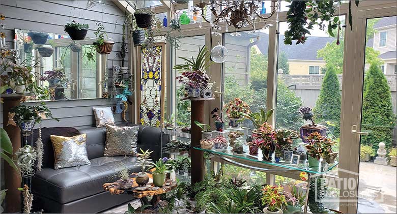 An inviting sunroom decorated with a sofa, plush throw pillows and potted plants and flowers. 