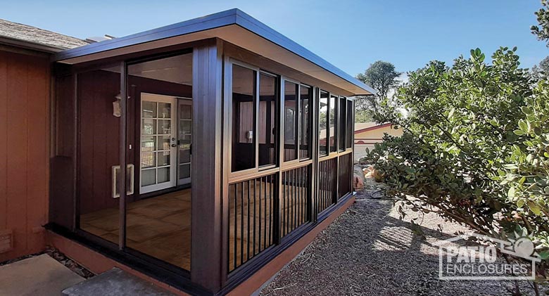 
 Three-quarter view of a brown screen room with picket railing along the front. Sliding screen doors are on the left. 