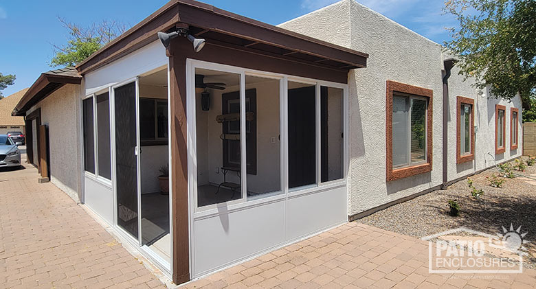 Beige Arizona room with solid knee wall and wood trim surrounded by patio pavers on a beige stucco home.