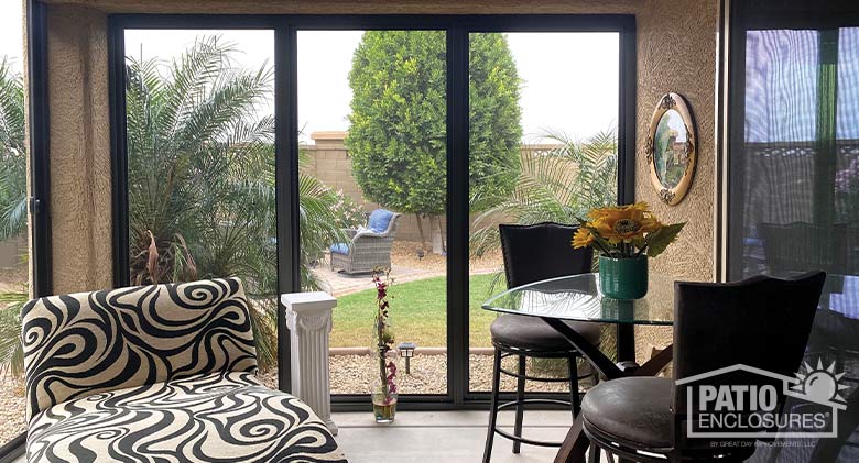 Interior of a screened Arizona room with black and tan print chaise on the left and tall table for two on the right.