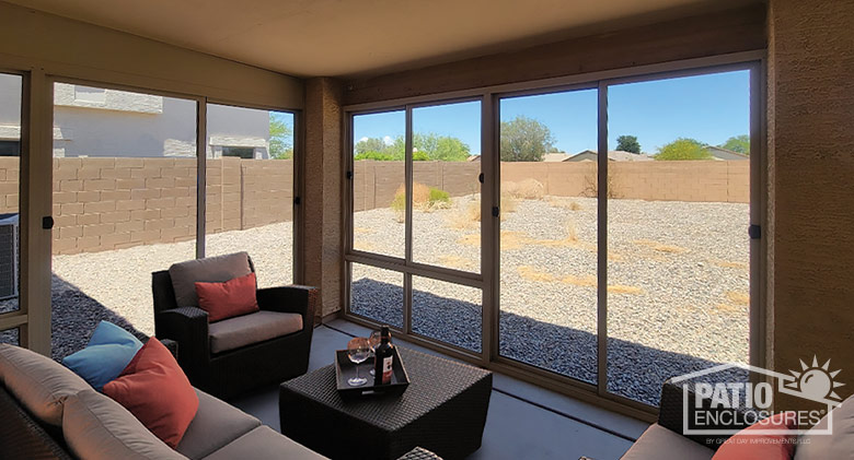 Interior of a screened Arizona room with cushioned wicker chairs and couch and a small coffee table. View of backyard.