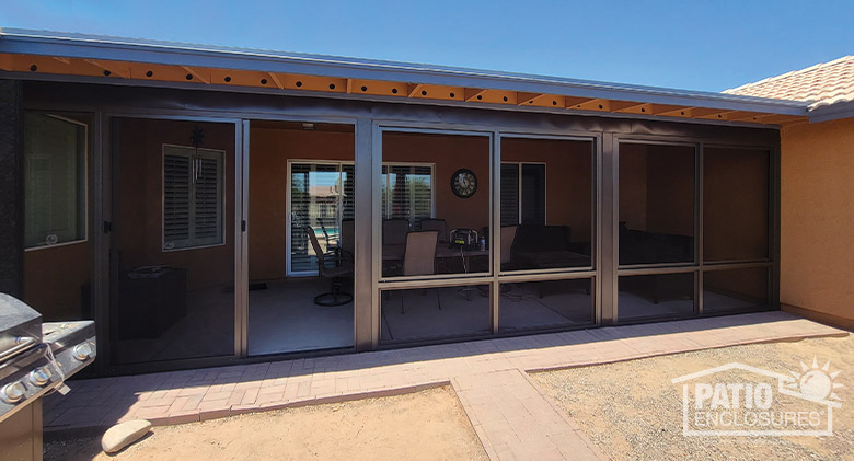 A covered patio screened enclosure with a brown frame and a grill in the foreground.