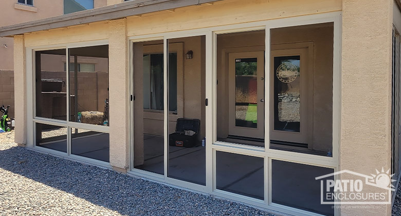 Arizona room screened porch enclosure with sliding screen doors in the middle on a beige stucco home.