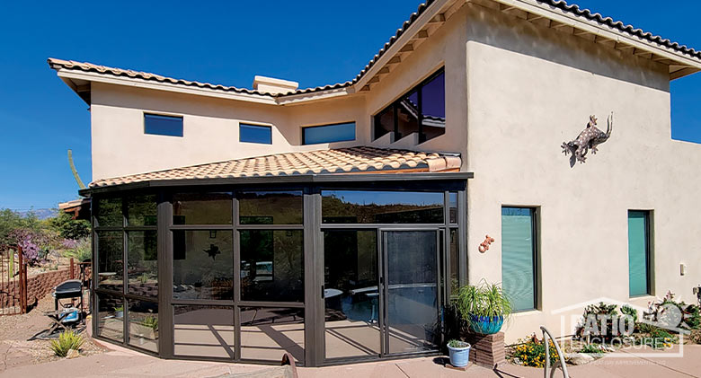 The exterior of a custom-shaped, rounded Arizona room enclosed in glass on a beige stucco home with patio.