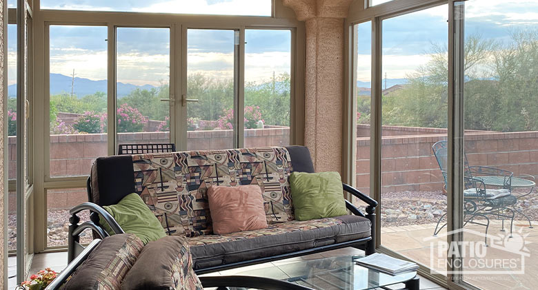 A patterned couch in earth tones in the interior of a glass-enclosed Arizona room with a view of the desert and mountains.