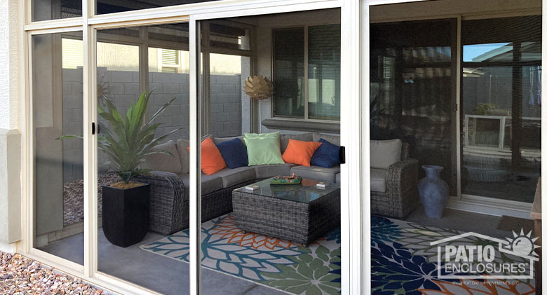 A view of the interior of a screened Arizona room with an L-shaped couch with bright pillows and a glass-topped coffee table.