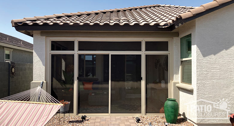 A brick walk leads to a screened corner patio on a stucco building with tile roof. A hammock and urn sit outside.