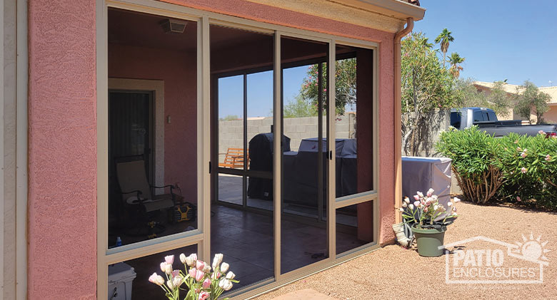 Exterior of a screened corner Arizona room on pink stucco house, potted tulips in front and trees and shrubs in background.