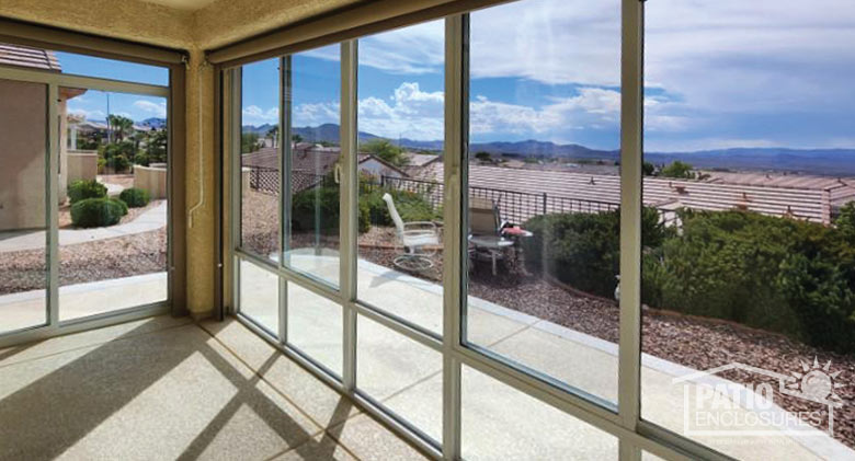 The sun streaming in through walls of glass in an Arizona sunroom. We have a view of rooftops and distant mountains.