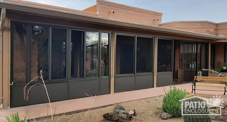 A screen room with brown framing and knee wall, and sliding doors on the right. Cacti and desert plants in the foreground.