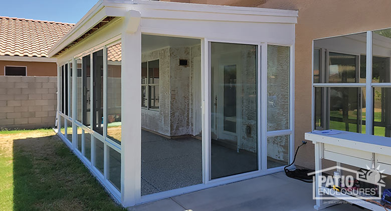 A covered patio enclosed with glass on three sides. The sunroom has a white frame, glass knee wall and patio door entry.