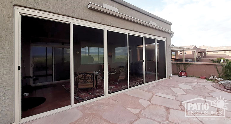 Exterior view of a screened Arizona room with a stone patio in front, and chairs and a rug inside.